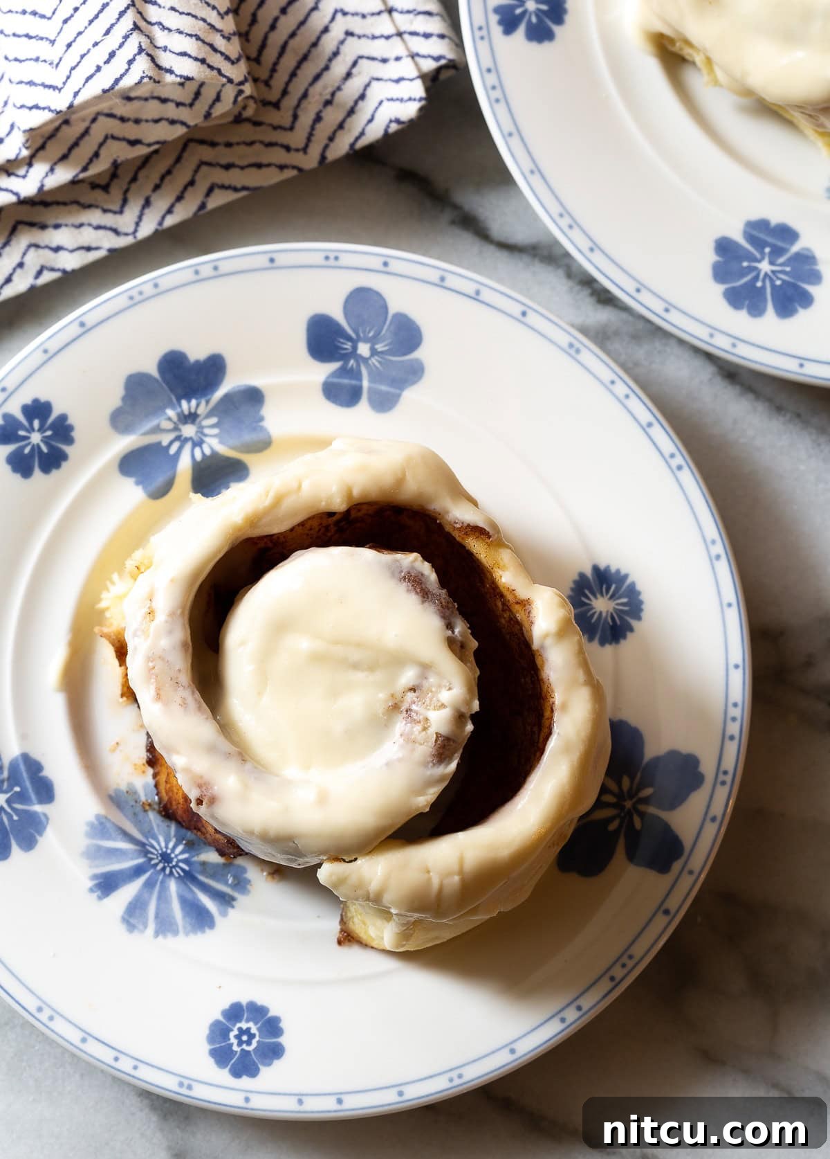 Overhead shot of a single perfectly iced Cinnabon-style cinnamon roll on a clean white plate.