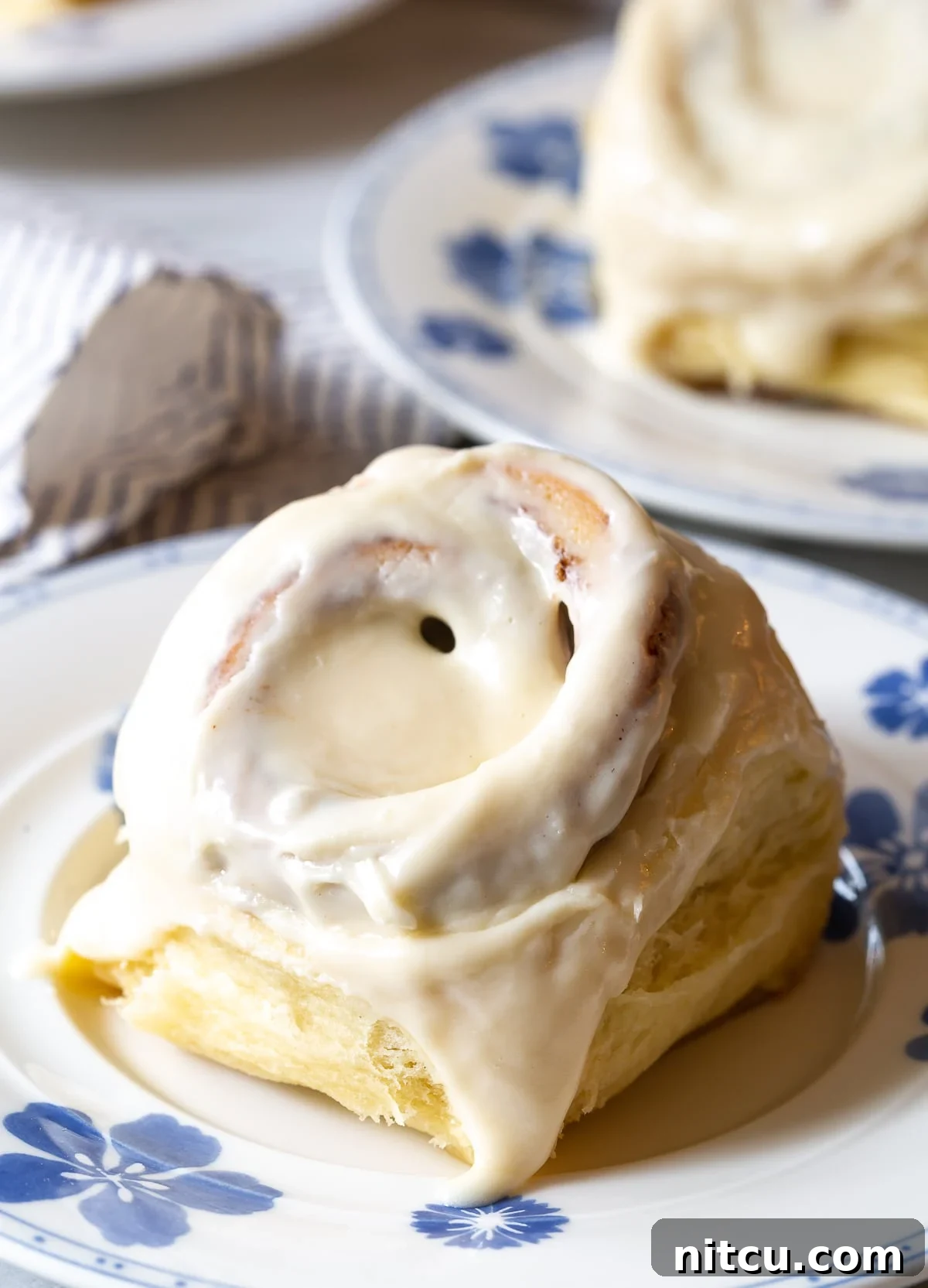 A single homemade Cinnabon-style cinnamon roll on a plate, topped with smooth cream cheese frosting.
