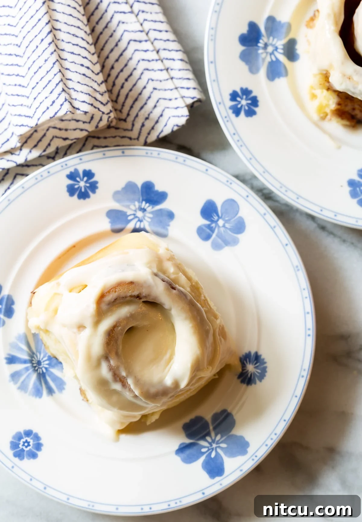 Overhead shot of two plates, each holding a perfectly baked and iced homemade cinnamon roll.