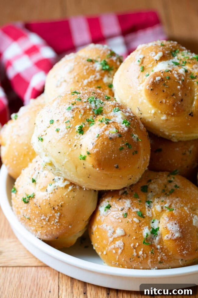 Garlic knots piled on top of each other on a white plate, showcasing their golden-brown crust and glistening garlic butter.