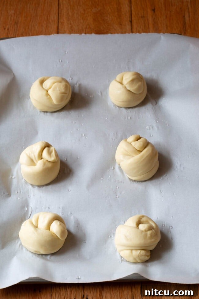 Garlic knots rising on a baking sheet, appearing plump and ready for their final bake.