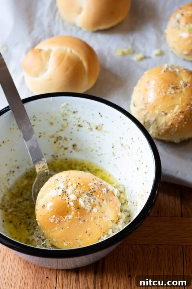 A close-up of a freshly baked garlic knot being dunked into a bowl of rich, melted garlic butter, ensuring every crevice is coated.