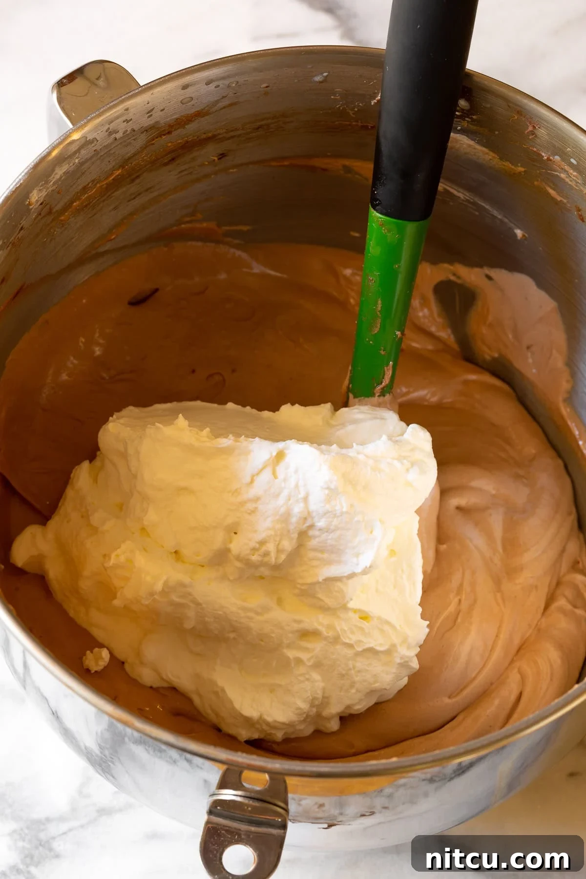 Whipped cream being gently folded into the rich chocolate filling mixture with a spatula.