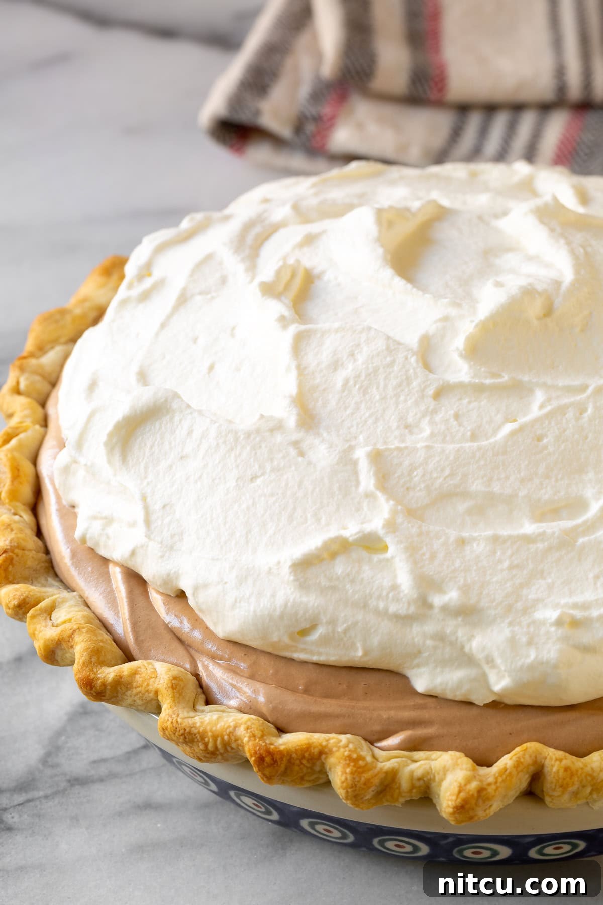 A completed pie crust filled with chocolate filling and topped with a generous layer of whipped cream.