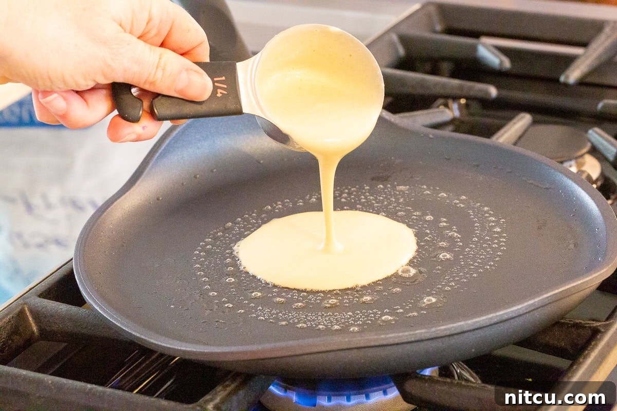 Pouring thin blini batter onto a hot crepe pan to make delicate pancakes