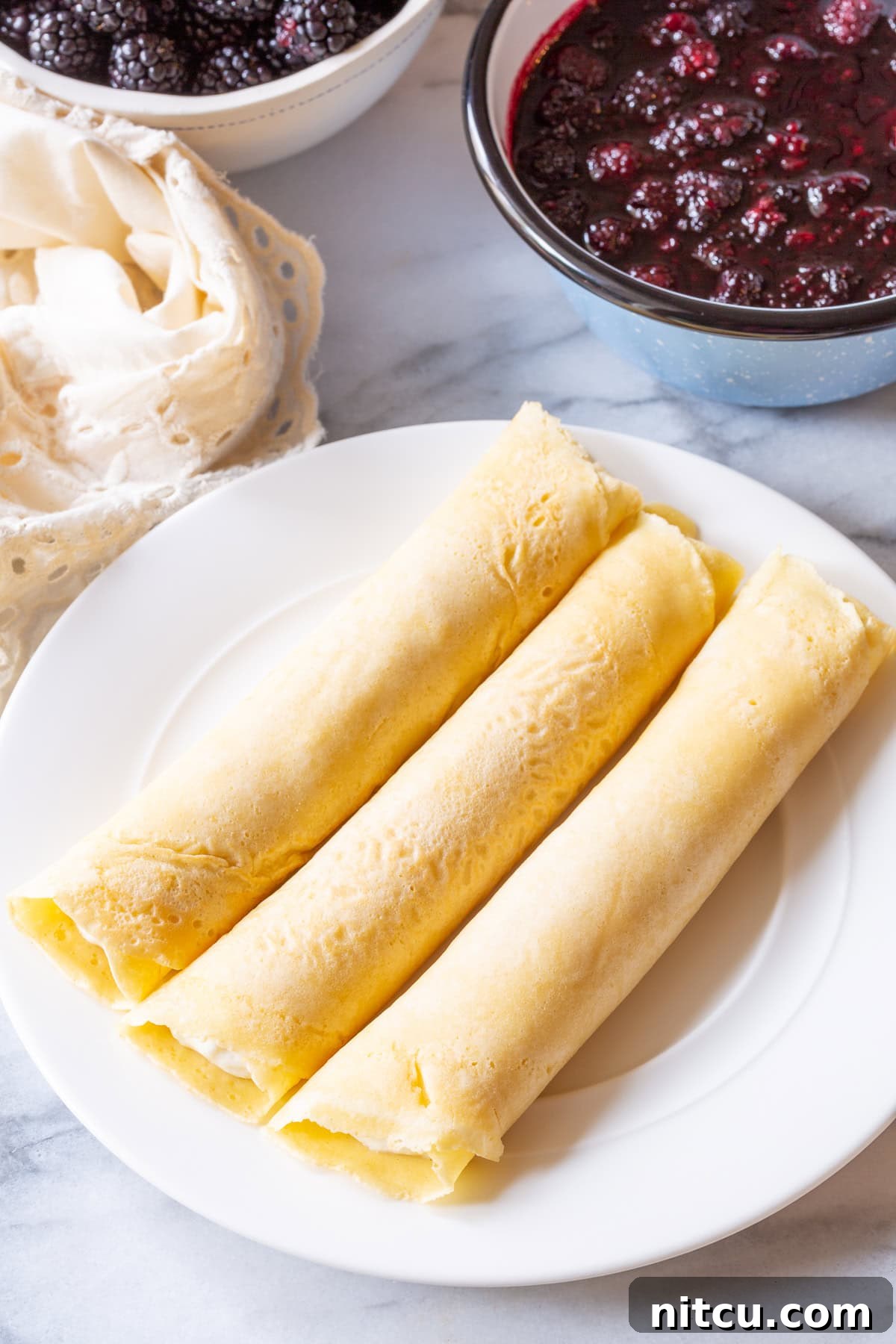 Rolling blintz pancakes around ricotta cream and stacking them neatly on a plate