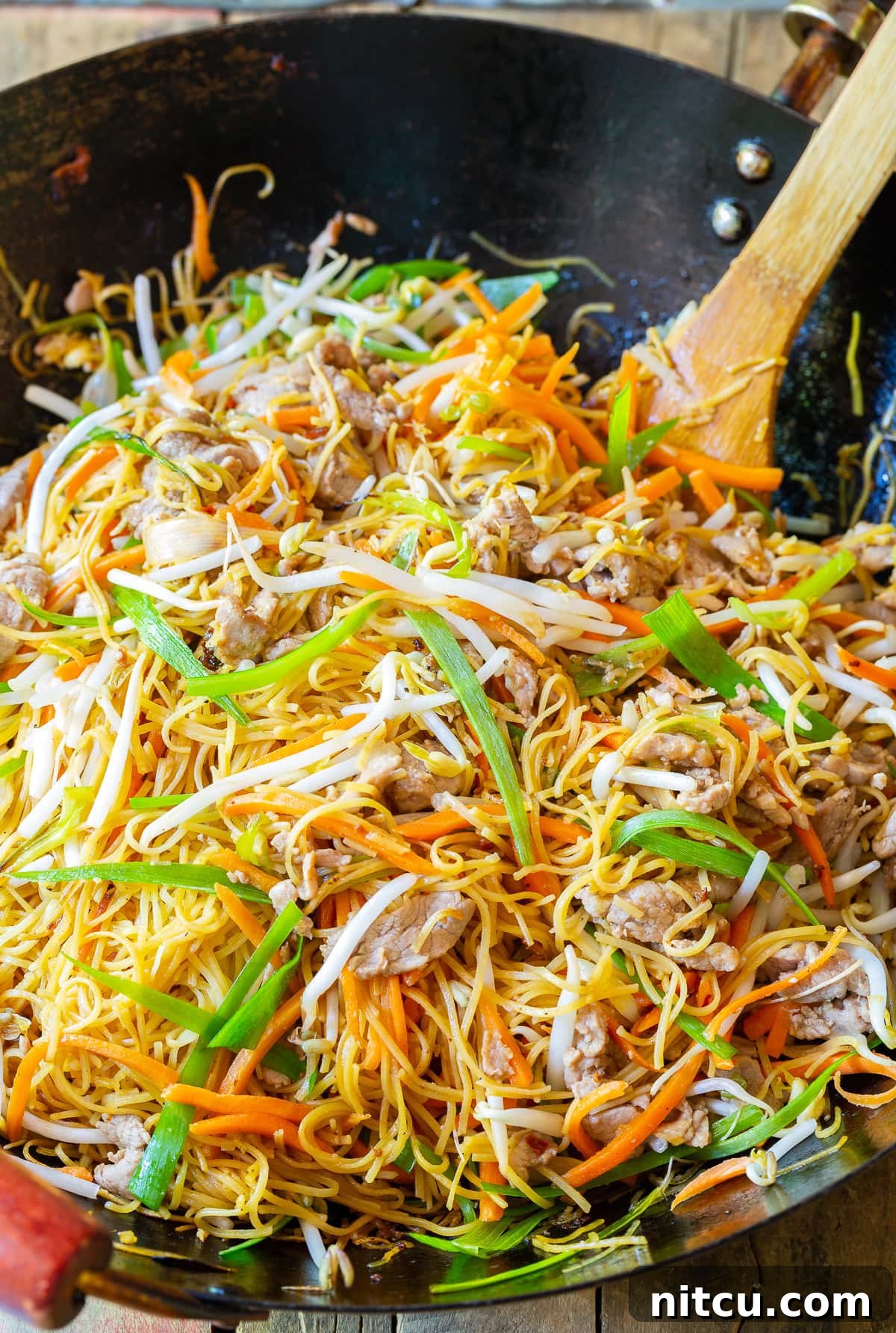 Close-up of Pork Lo Mein (Cantonese Noodles) being stir-fried in a traditional wok, showcasing the steam and rich colors of the ingredients.