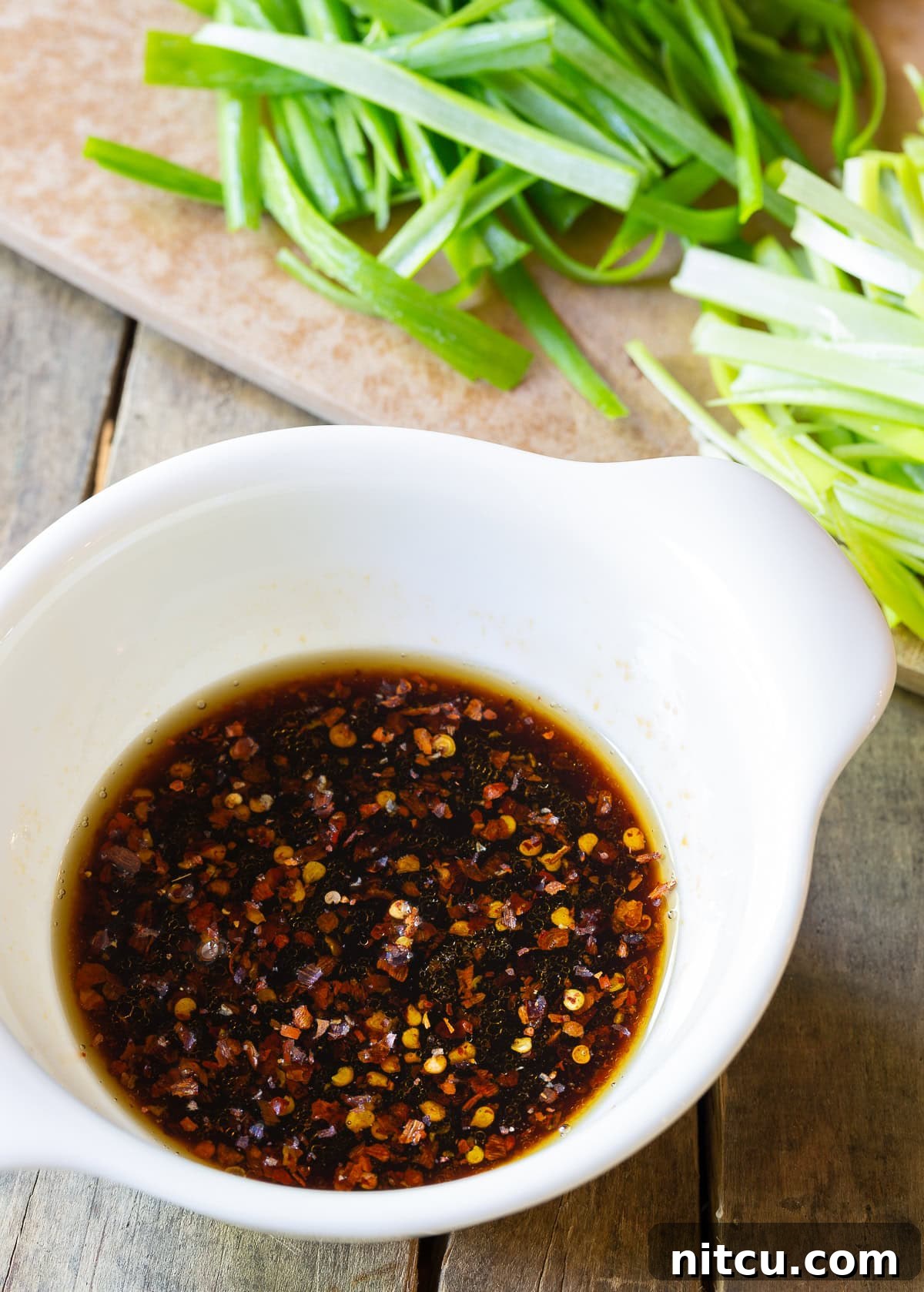 A small white bowl filled with the rich, dark, and flavorful sauce mixture for pork lo mein, ready to be added to the stir-fry.