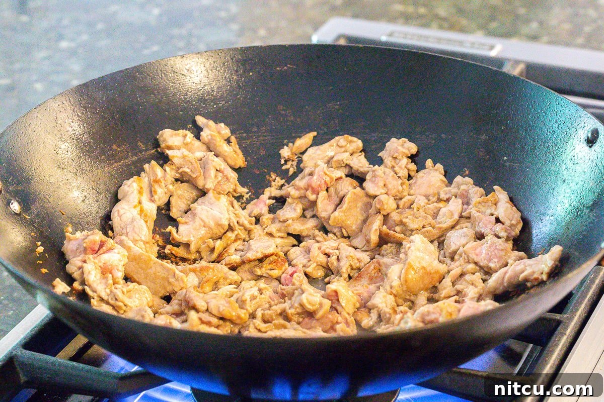 Thinly sliced pork loin searing in a large, hot wok, caramelizing beautifully for the Cantonese Noodles.