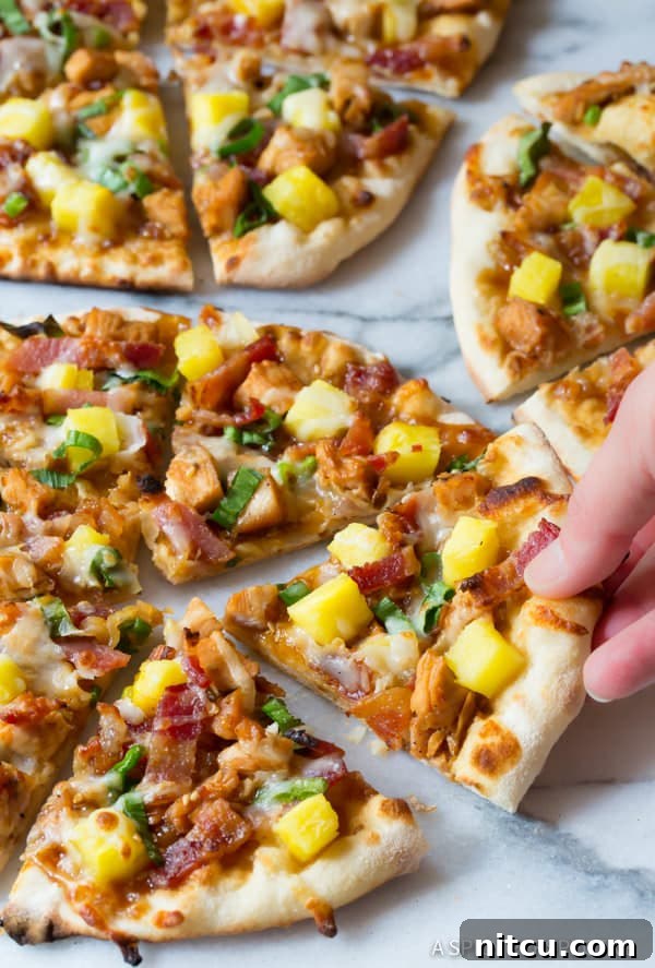 Closeup of hand removing a slice of delicious grilled teriyaki chicken pizza with pineapple and bacon.