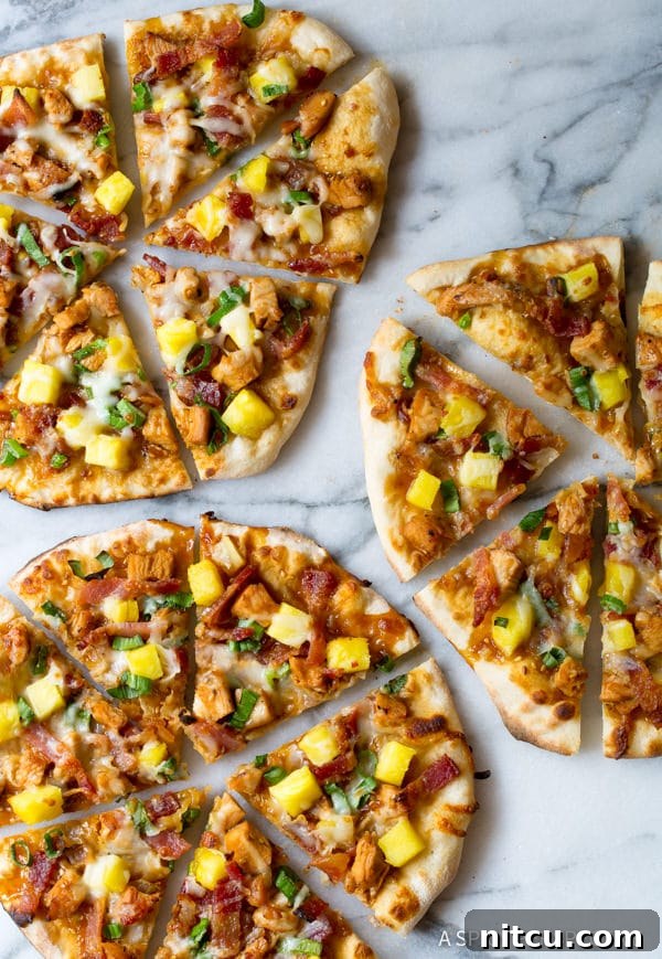Overhead shot of Teriyaki Chicken Pizza slices with fresh pineapple and melted cheese on a white backdrop.