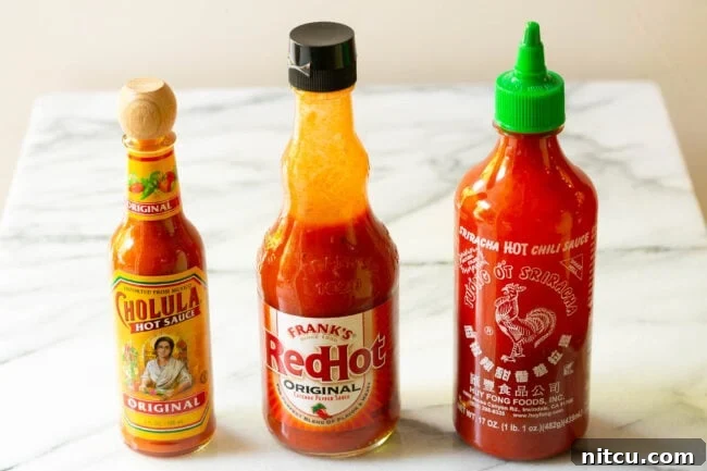 Three distinct bottles of hot sauce lined up neatly on a pristine marble countertop, ready for use.