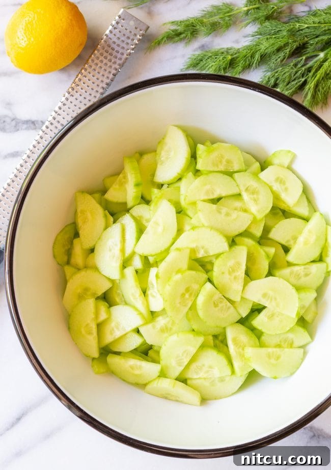 Top view of thinly sliced English cucumbers, perfectly halved and ready for mixing in a large bowl, showcasing their crisp texture.