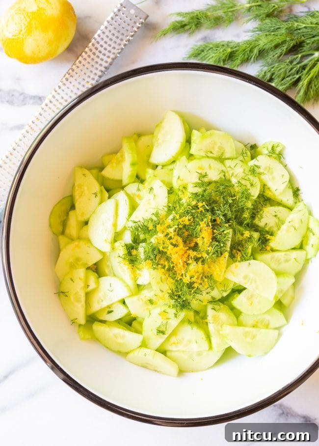 A candid shot of sliced cucumbers being gently tossed with creamy dill dressing in a mixing bowl, illustrating the preparation process.