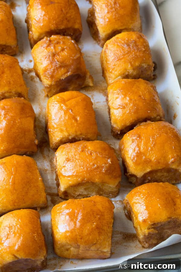 Unbaked cinnamon buns being dunked in butter, showing the coating process.