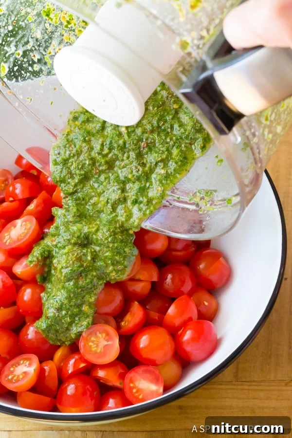 Pouring the green sauce from the food processor over a bowlful of halved cherry tomatoes.