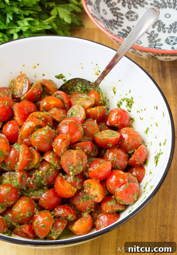 Using a large metal spoon to stir the tomato salad in a white bowl.