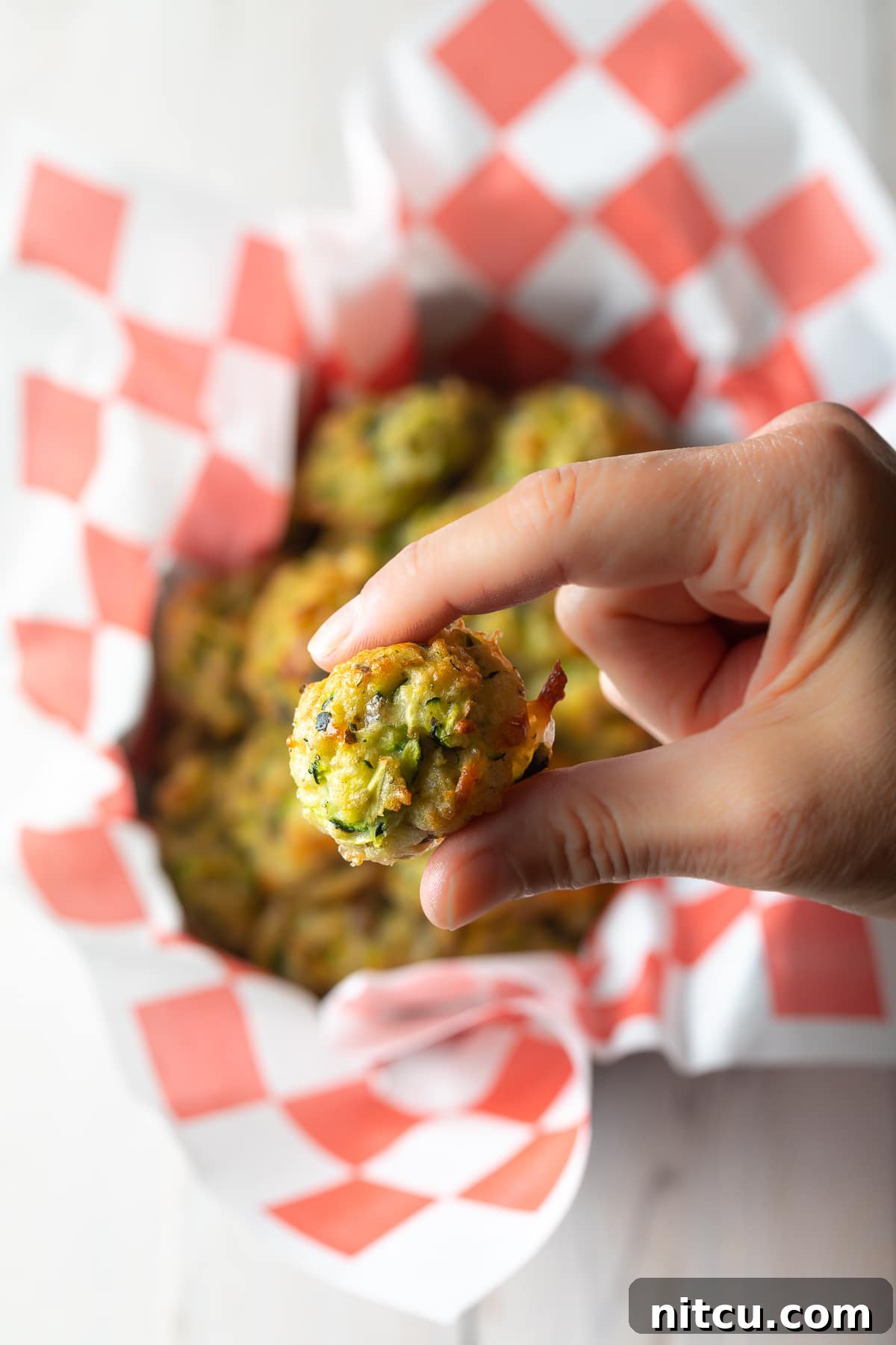 A hand gently holds a perfectly baked zucchini tot, showcasing its golden-brown texture.