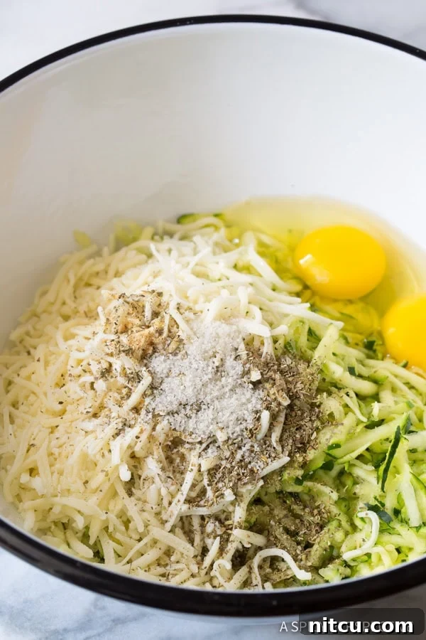 A bowl filled with fresh ingredients for zucchini tots, including shredded zucchini, cheese, and spices.