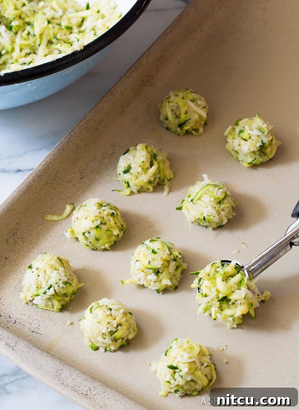 Uniform balls of zucchini tot mixture perfectly spaced on a parchment-lined baking sheet, ready for the oven.