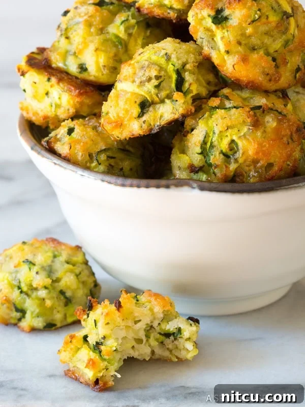 A close-up of a half-eaten baked zucchini tot, revealing its tender, cheesy interior and crispy crust.