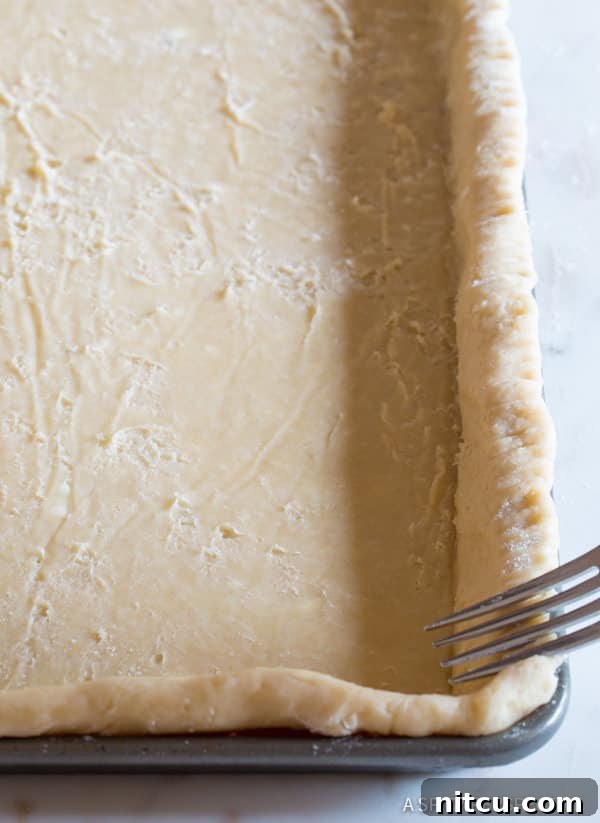 Crimping the edges of a homemade pie crust in a cookie sheet, a crucial step for a beautiful slab pie.