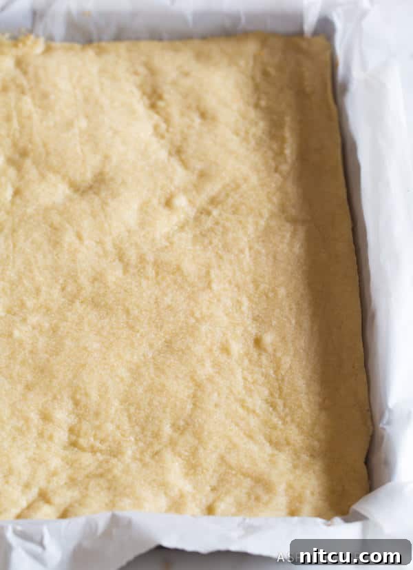 Buttery shortbread cookie crust resting in a baking pan, perfectly lined with parchment paper.