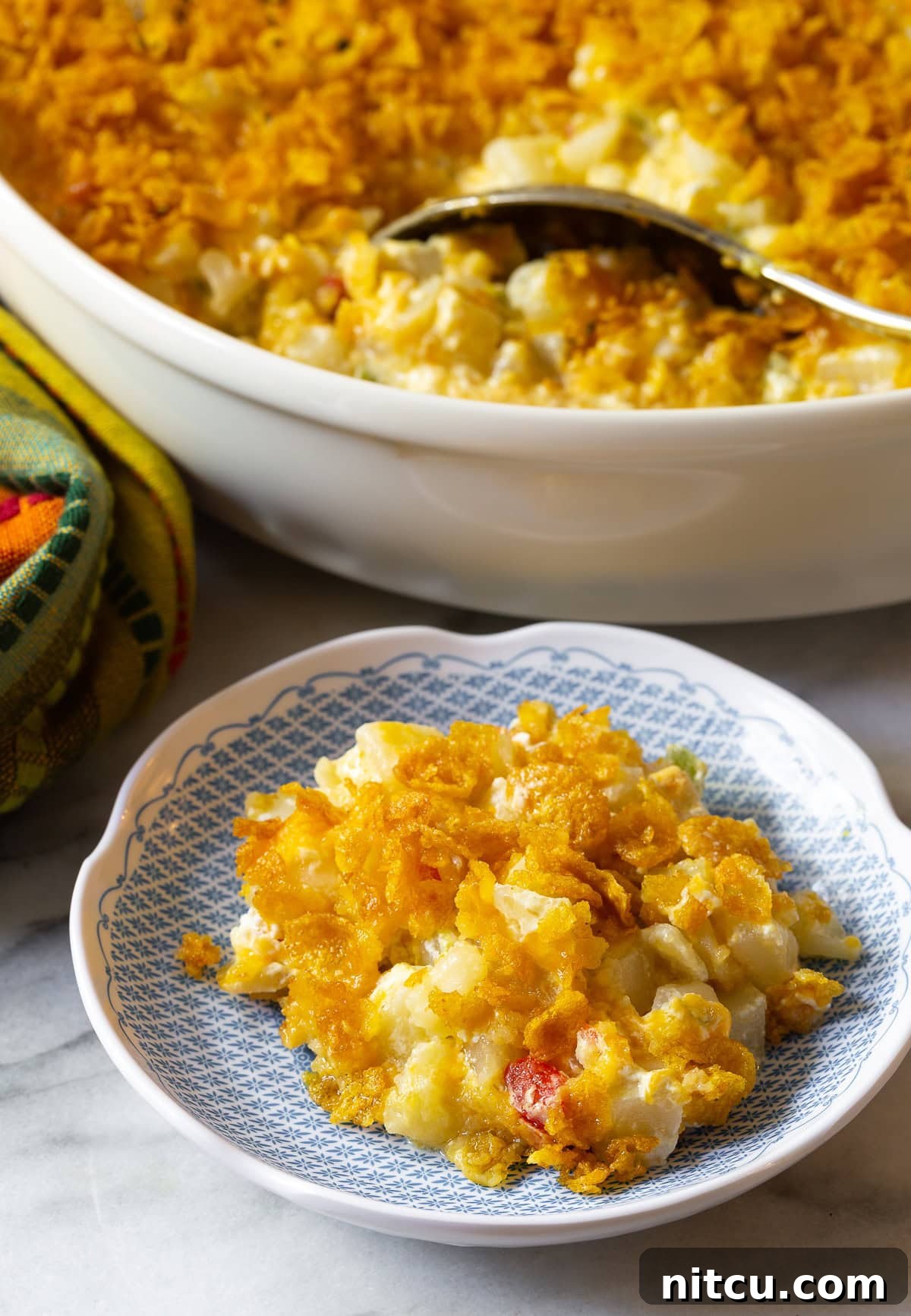 Spoon in dish with creamy potatoes hiding under crispy top on blue plate.