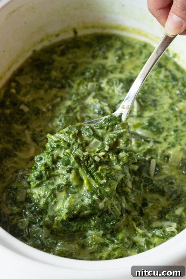 Creamed spinach in a crock pot with a large spoon taking a scoop.