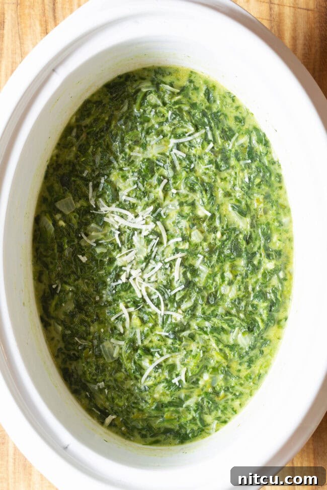 Crockpot with loaded creamy spinach topped with grated parmesan.
