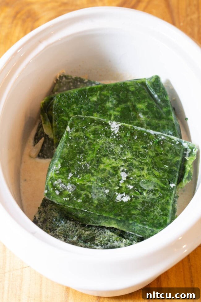 Frozen Spinach is placed in the slow cooker on top of the onions and cream mixture.