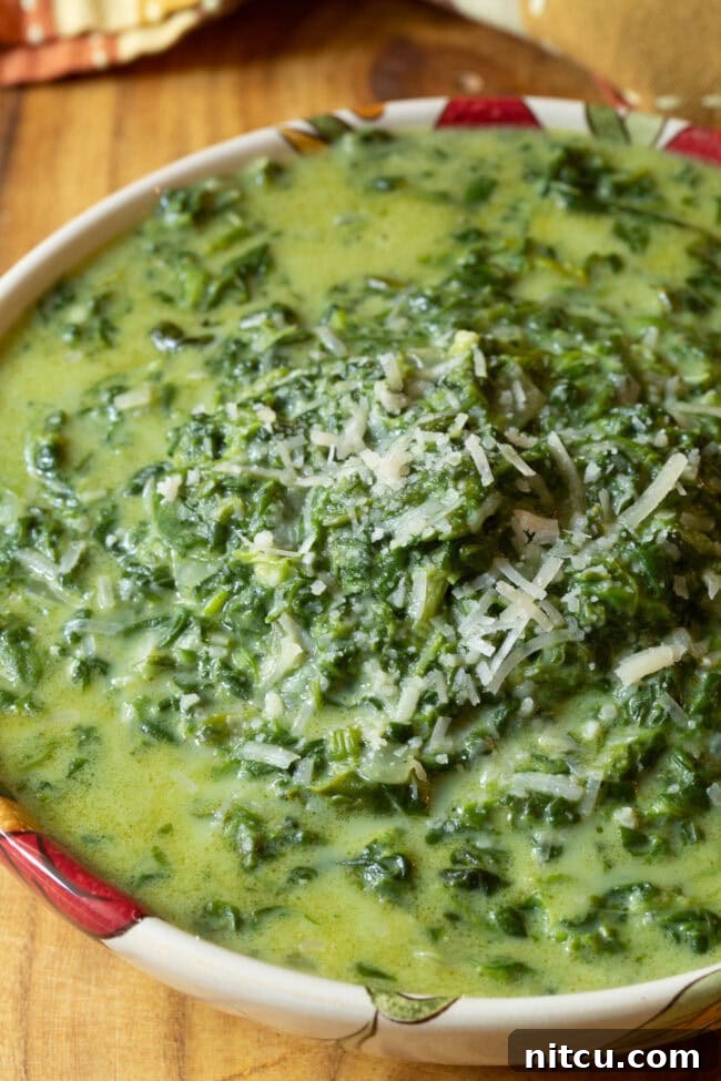 Slow Cooker Creamed Spinach with some cheese sprinkled on top in a serving bowl.