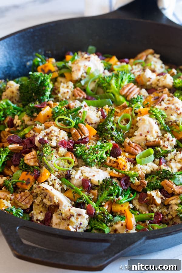 Chicken Broccoli Quinoa Skillet Recipe, a close-up shot in the pan, garnished with crunchy nuts and fresh scallions, inviting diners to taste its rich texture and flavor.