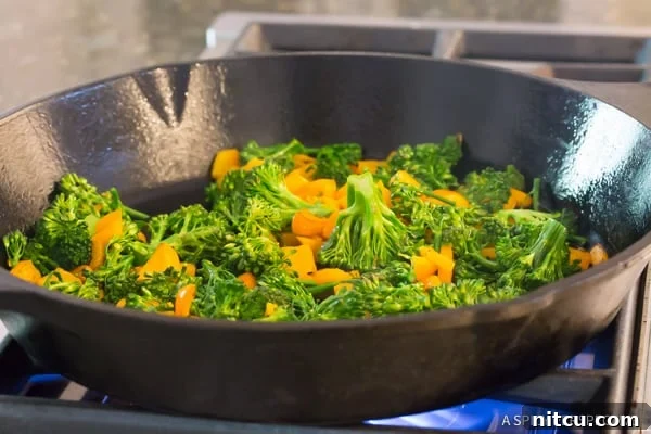 Fresh broccoli florets cooking in a hot pan, starting to soften and blister around the edges, preparing for the delicious Chicken Broccoli Quinoa Skillet.