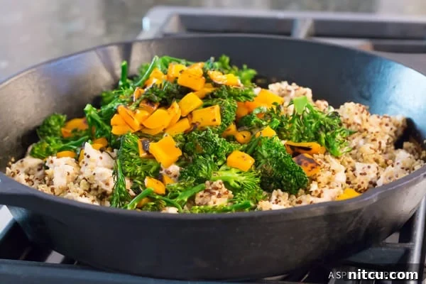 Chicken Broccoli Quinoa - adding colorful sautéed vegetables, dried cranberries, and pecans back into the pan with the cooked chicken and quinoa, for the final mix.