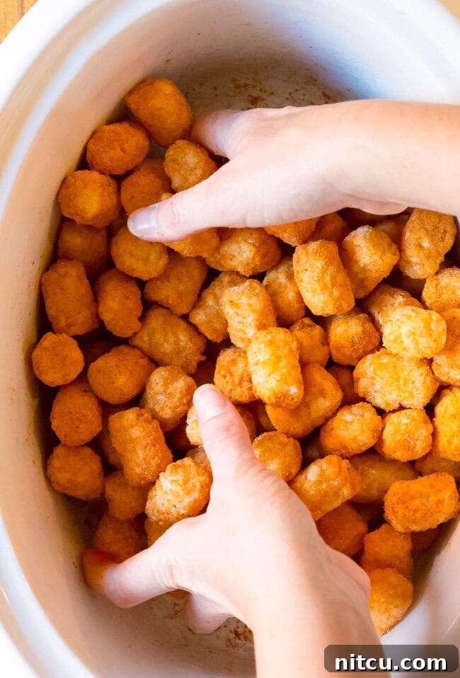 Hands mixing up frozen tater tots and taco seasoning in a baking dish. 