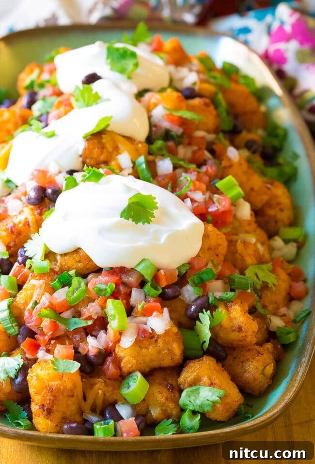 Slow cooker taco tater tots with toppings on a serving platter. 