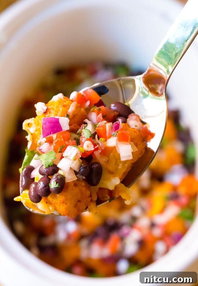 Spoonful of taco tater tots and other toppings with the rest of the tater tots in the background. 