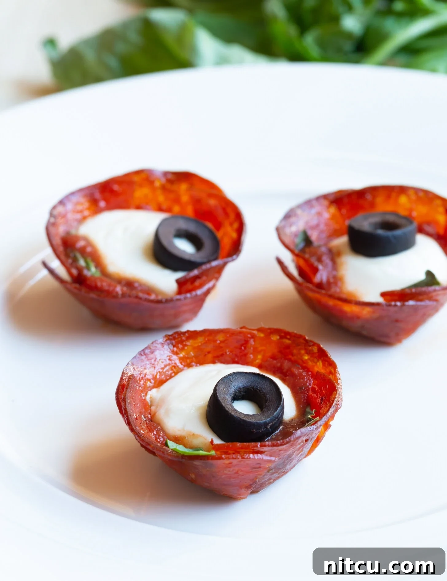 A plate brimming with golden-brown, cheesy pepperoni cups, garnished with vibrant green basil and savory black olives, ready to be served as an irresistible appetizer.