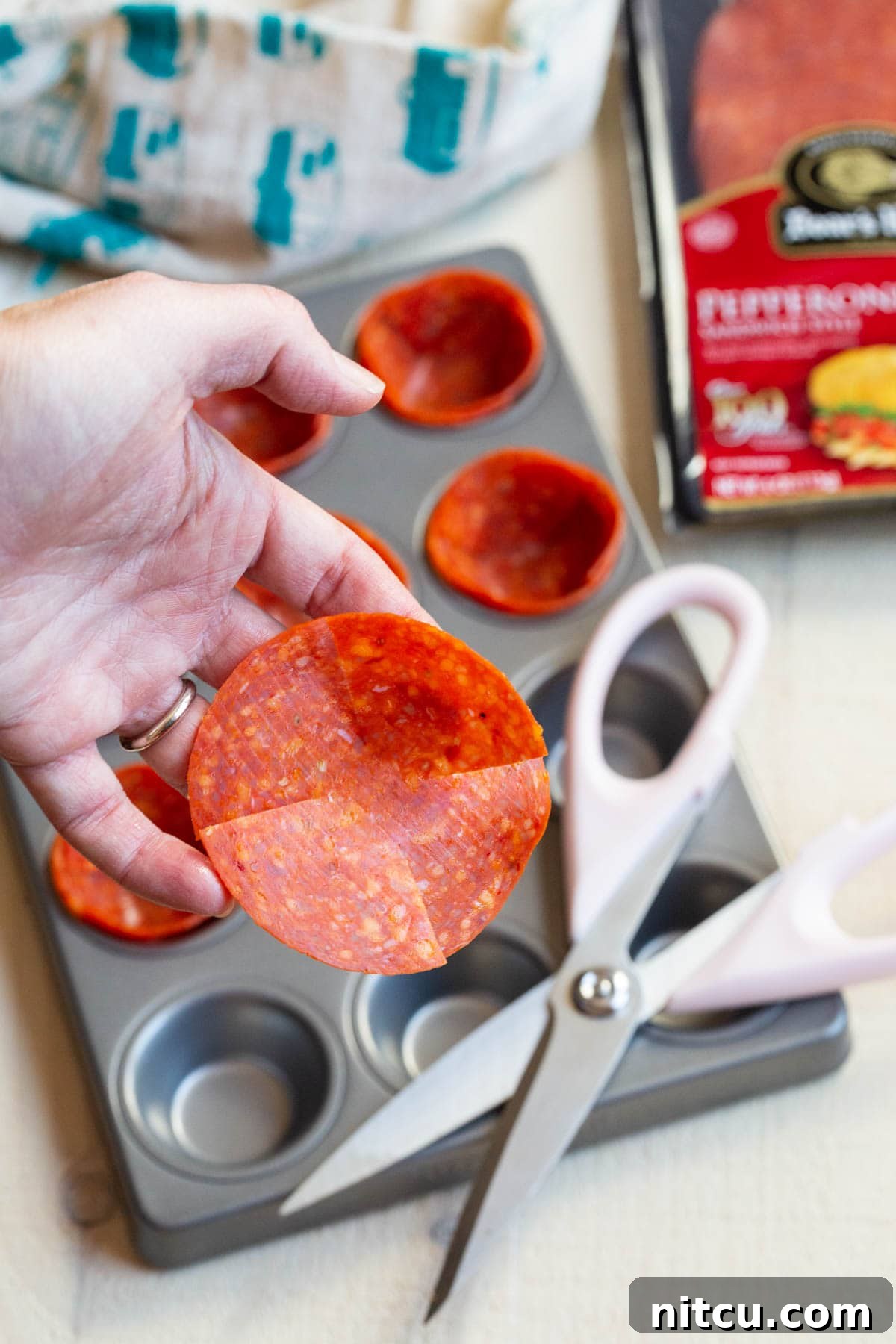 A hand holds a large pepperoni slice, expertly cut with kitchen scissors to create four slits around the edge, ready to be shaped into a cup.