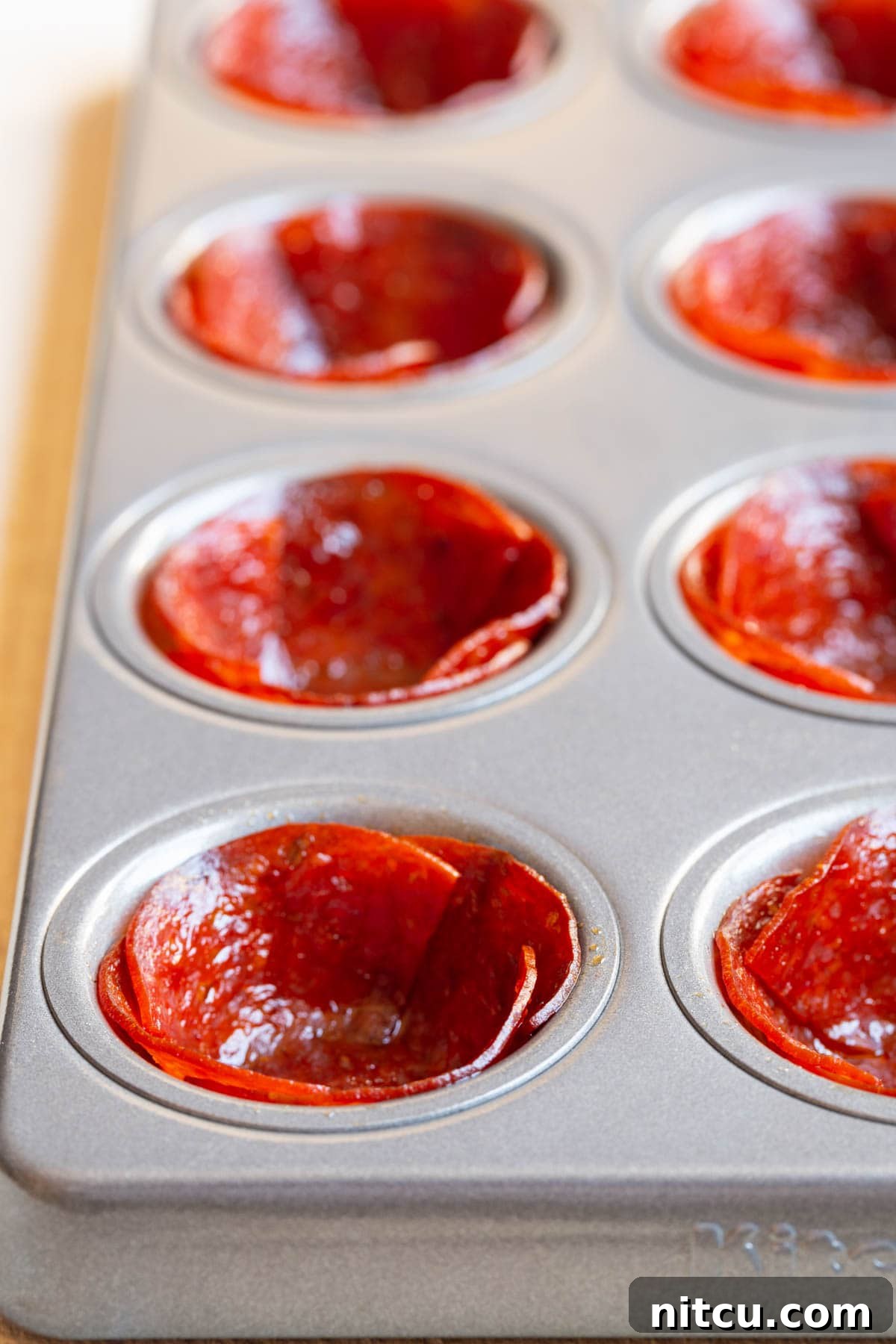 A mini muffin tin filled with perfectly baked, crispy pepperoni shells, ready for their delicious fillings.