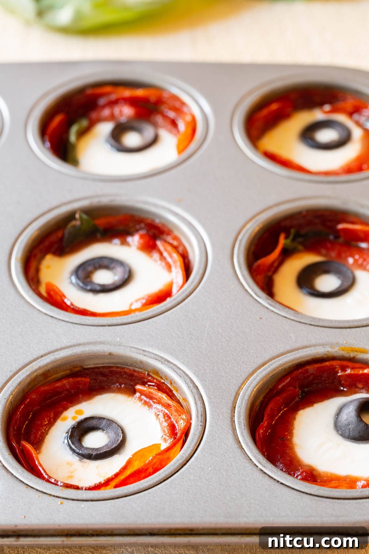 A vibrant close-up of baked pepperoni cups, their cheese perfectly melted and bubbly, garnished with fresh basil leaves, hot and ready to serve.