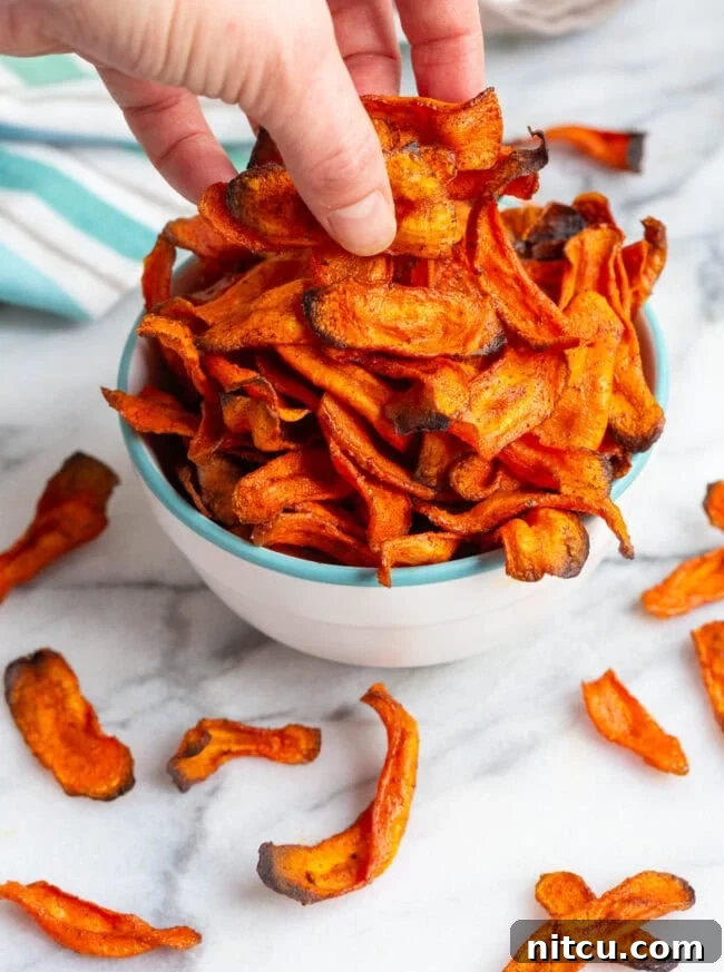 A hand reaching into a bowl to grab a handful of delicious carrot chips.