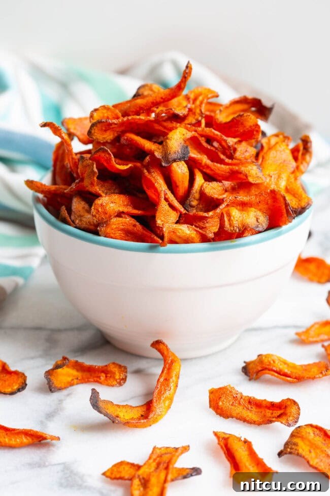 Baked carrot chips arranged beautifully in a bowl, with some scattered around it.