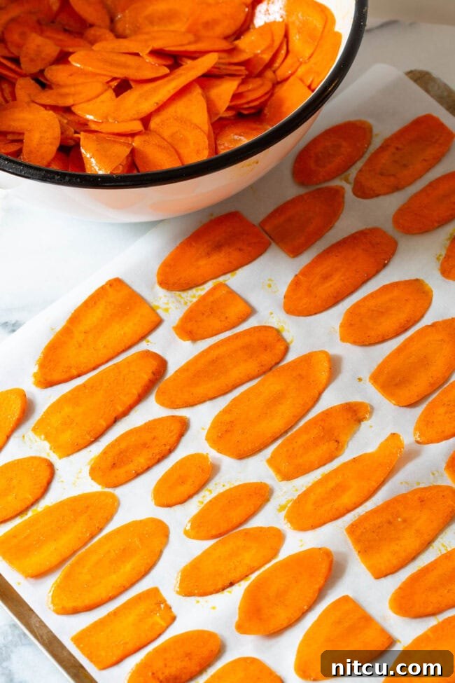 Seasoned carrot slices spread in a single layer on a baking sheet.