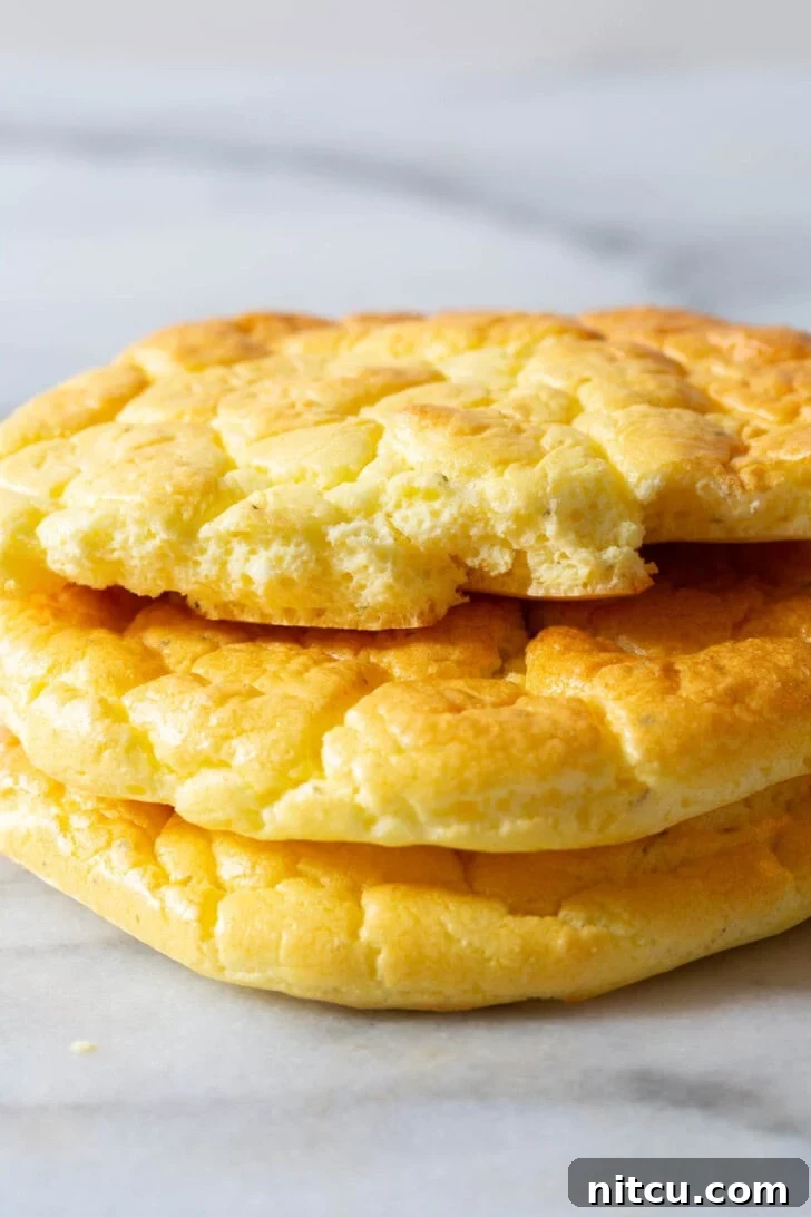 Multiple pieces of cloud bread stacked, with one torn in half to reveal its soft, airy interior, showcasing its perfect texture.