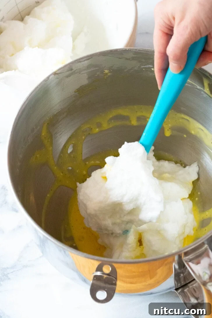 The process of gently folding whipped egg whites into the rich egg yolk mixture, demonstrating a key step for airy cloud bread.