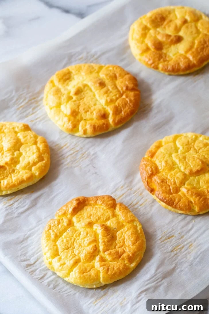 Freshly baked cloud bread cooling on a baking sheet lined with parchment paper, showcasing its golden finish.