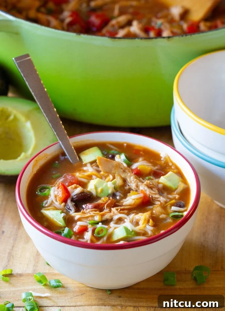 Soup in a bowl garnished with melted shredded cheese, vibrant sliced scallions, and creamy diced avocado, ready to be enjoyed.