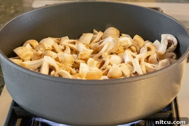 Diced mushrooms being cooked in a skillet on the stove. 